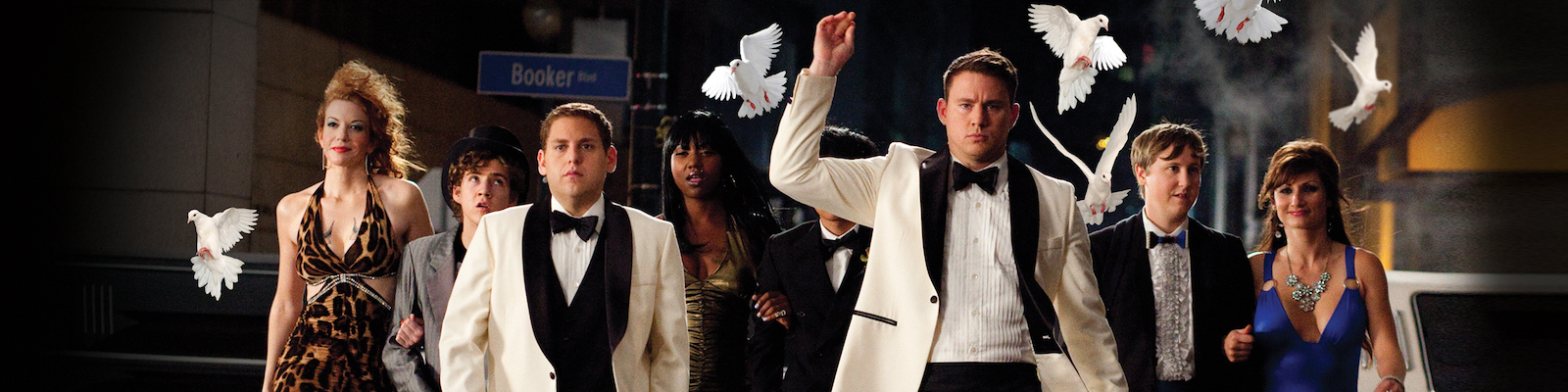 a group of young people in formal prom outfits walk down a dark city street as doves fly in the background in 21 jump street