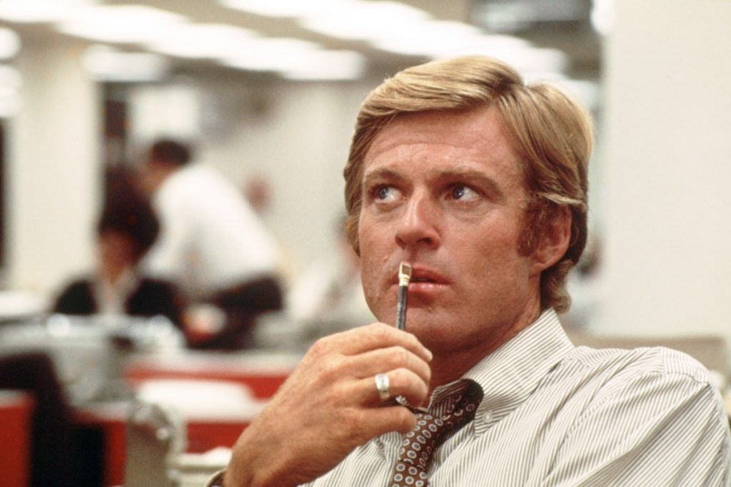 Robert Redford as Bob Woodward sits at a desk in All the President's Men