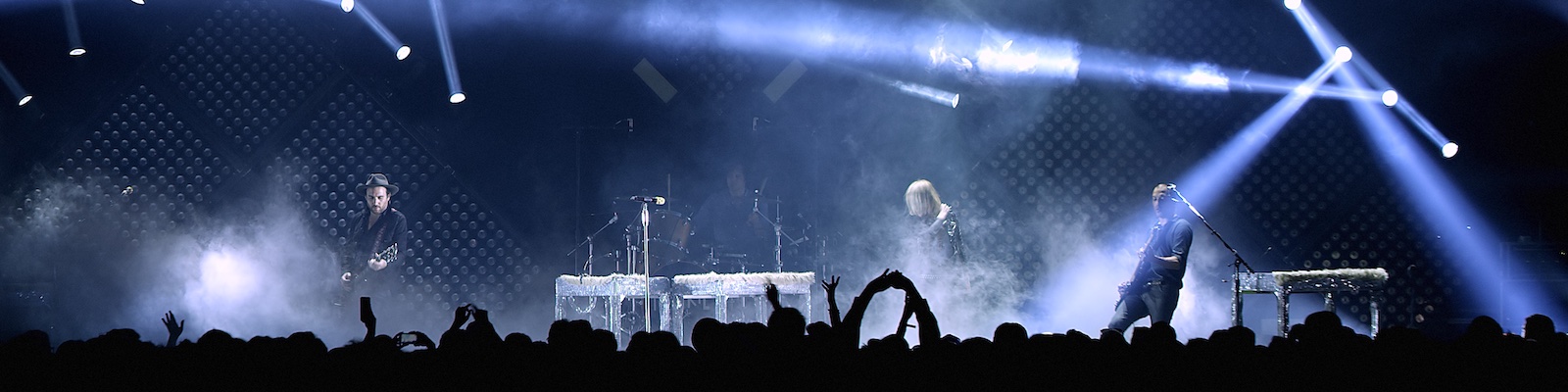 spotlights cross a stage as the rock band Metric performs in front of an audience