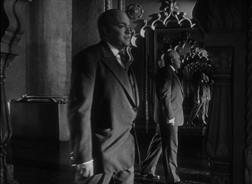 As Orson Welles as Charles Foster Kane walks through a room, his image is reflected endlessly in two mirrors facing eachother 