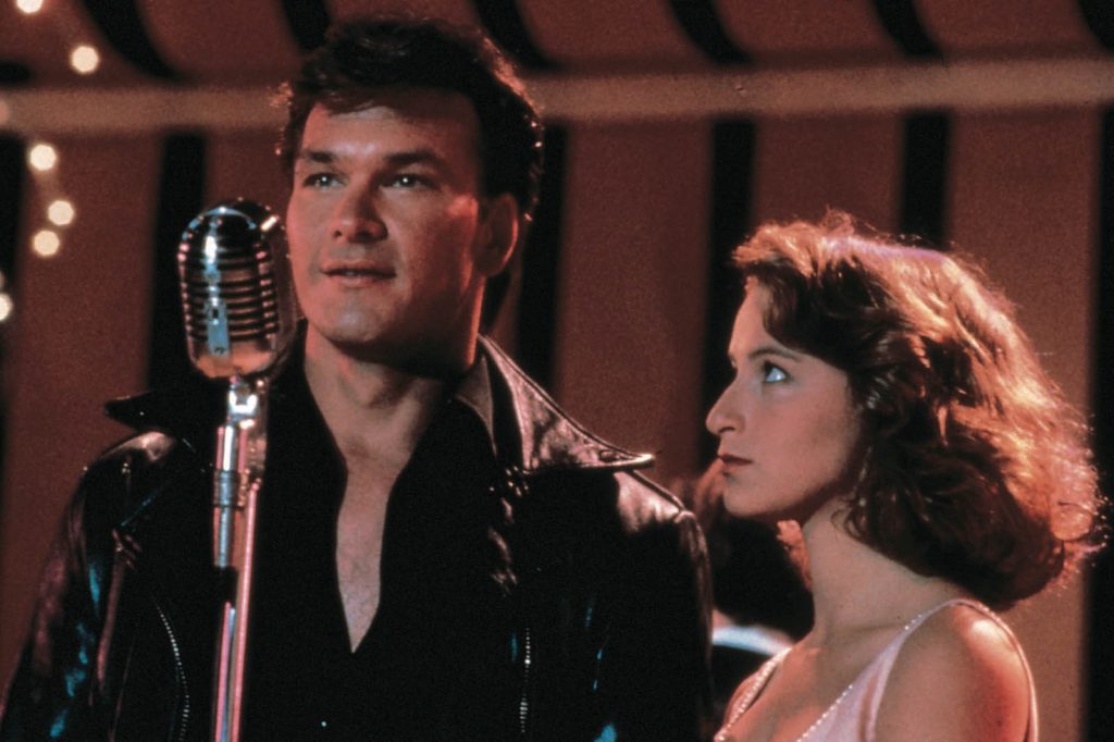 Patrick Swayze and Jennifer Grey stand at a microphone in Dirty Dancing
