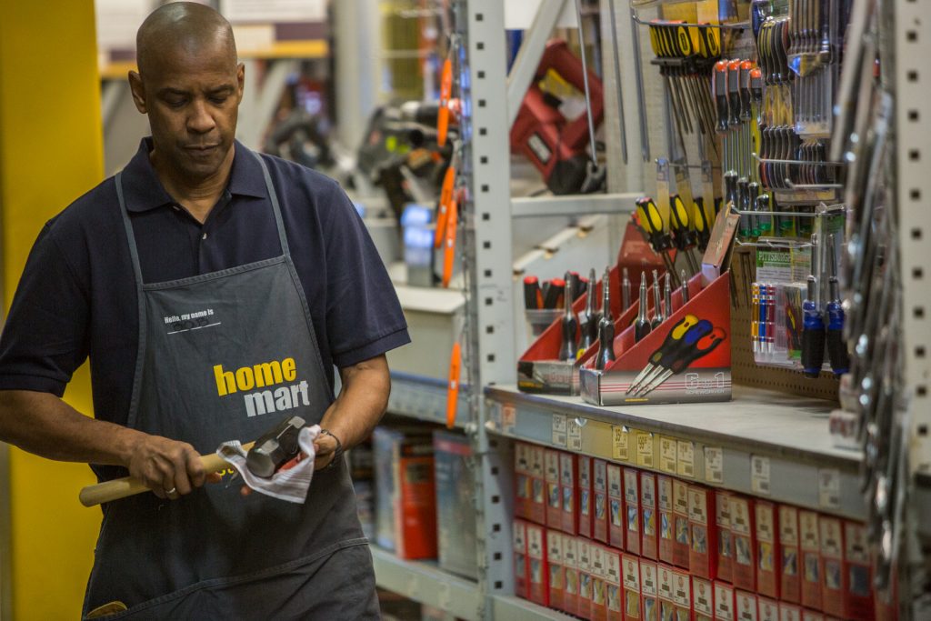 Denzel Washington stands in a hardware store holding a hammer