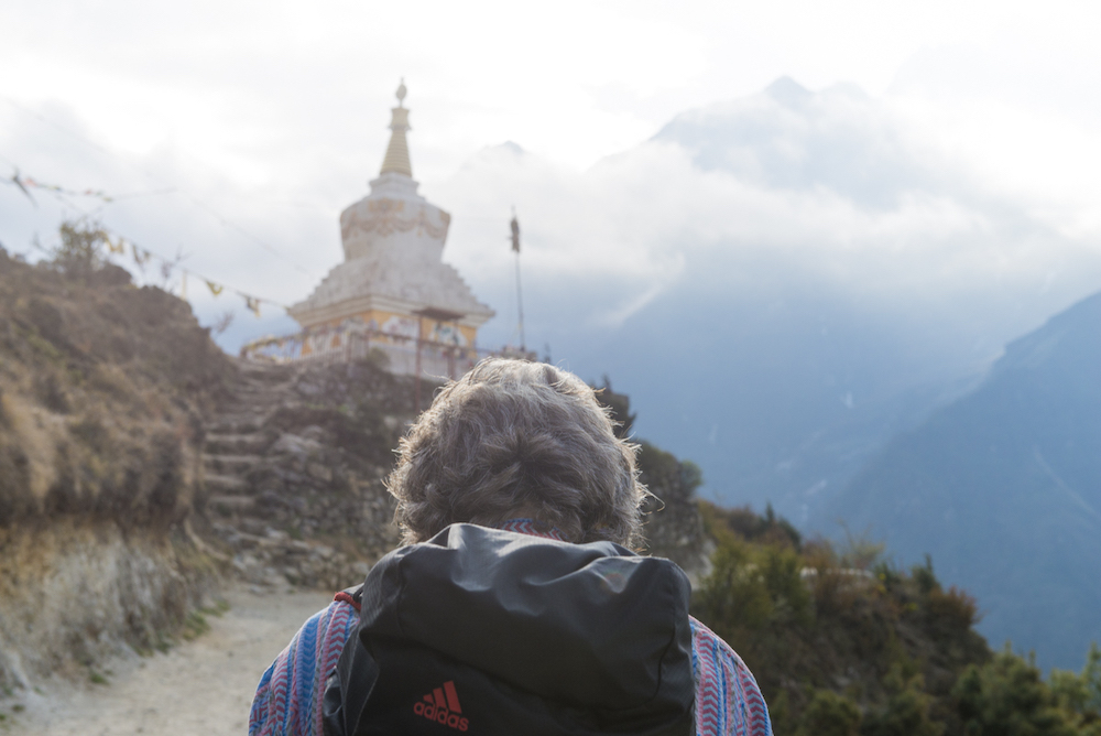 (from behind) a person climbs to a holy site with a mountain looming in the distance