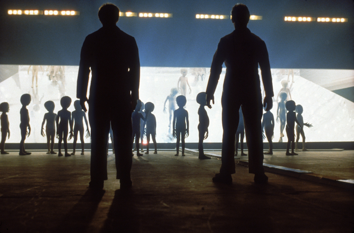 two human figures and a large number of small alien figures in silhouette 