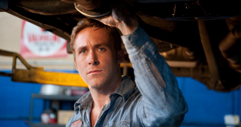 Ryan Gosling stands under a car that has been raised in a garage in Drive
