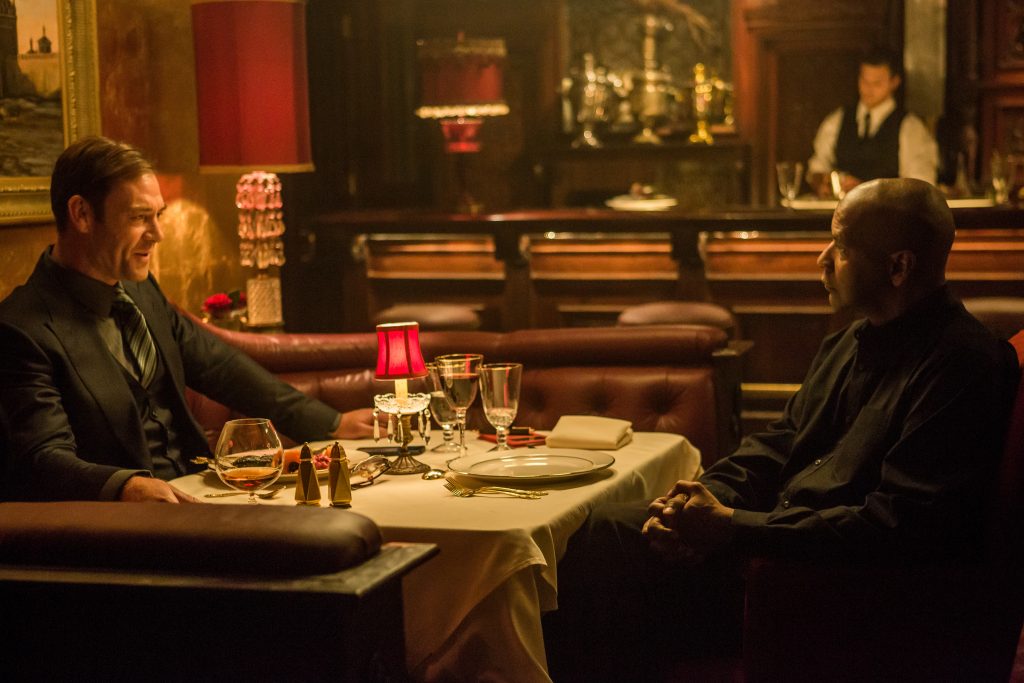 Marton Csokas and Denzel Washington sit at a table in a dimly lit restaurant 