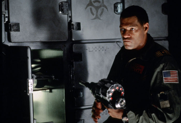 Laurence Fishburne, in a jumpsuit with an American flag, retrieves an item from a locker in Event Horizon