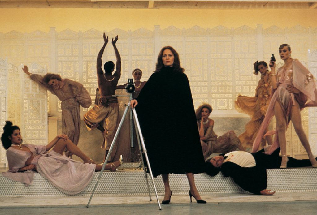 Faye Dunaway as Laura Mars poses with models and her camera on a tripod