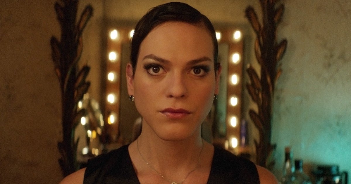A white woman with dark, slicked down hair looks into the camera in front of a mirror ringed with lightbulbs (A Fantastic Woman)