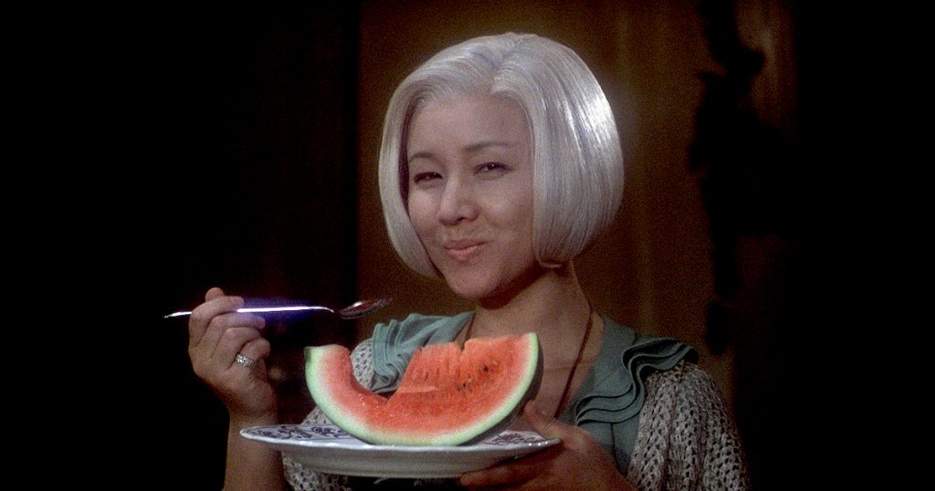An older woman smiles as she eats a slice of watermelon
