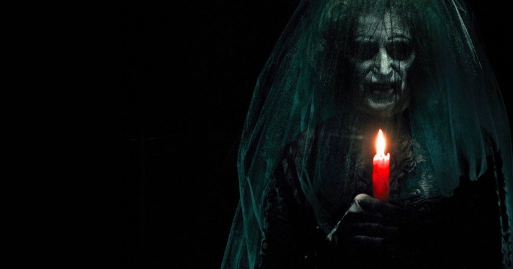 A hideous witch wearing a veil holds a lit candle in Insidious