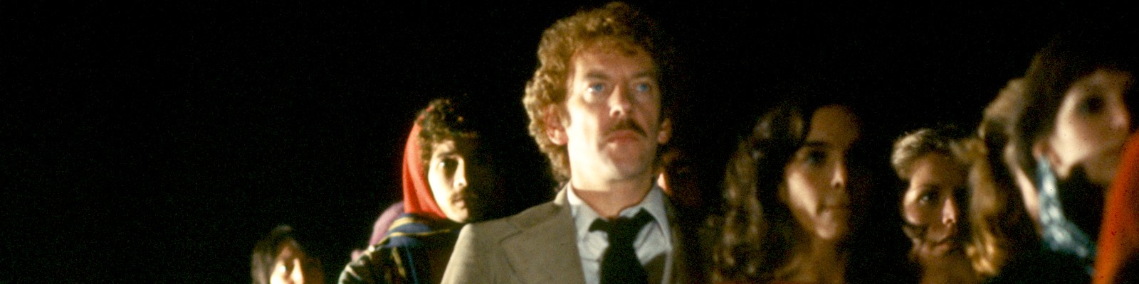 Donald Sutherland stands in a line of people in the dark in Invasion of the Body Snatchers