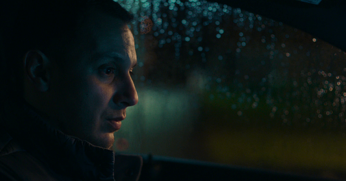 Side image of a man sitting in a car on a rainy night