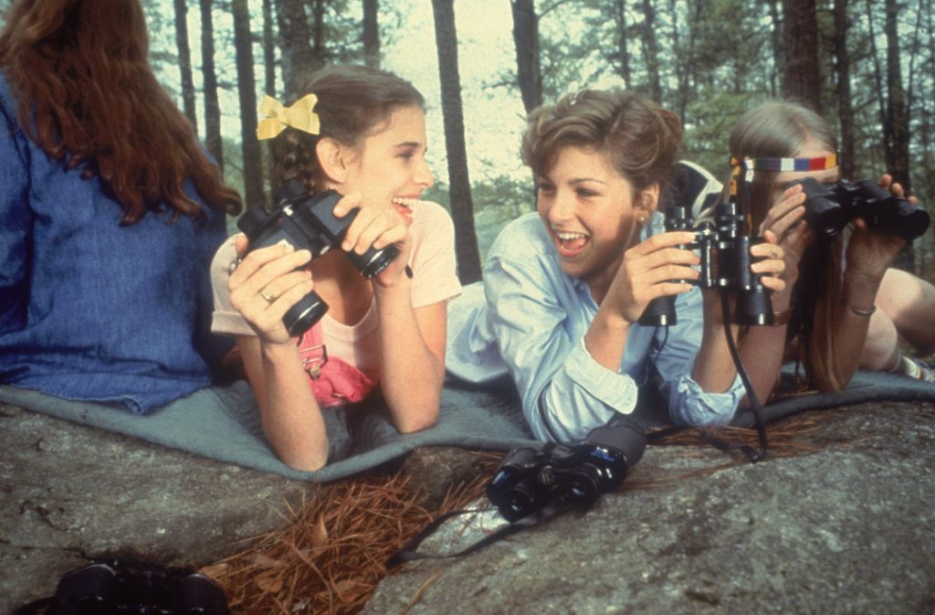 Female campers smile and laugh as they spy on other girls in Little Darlings