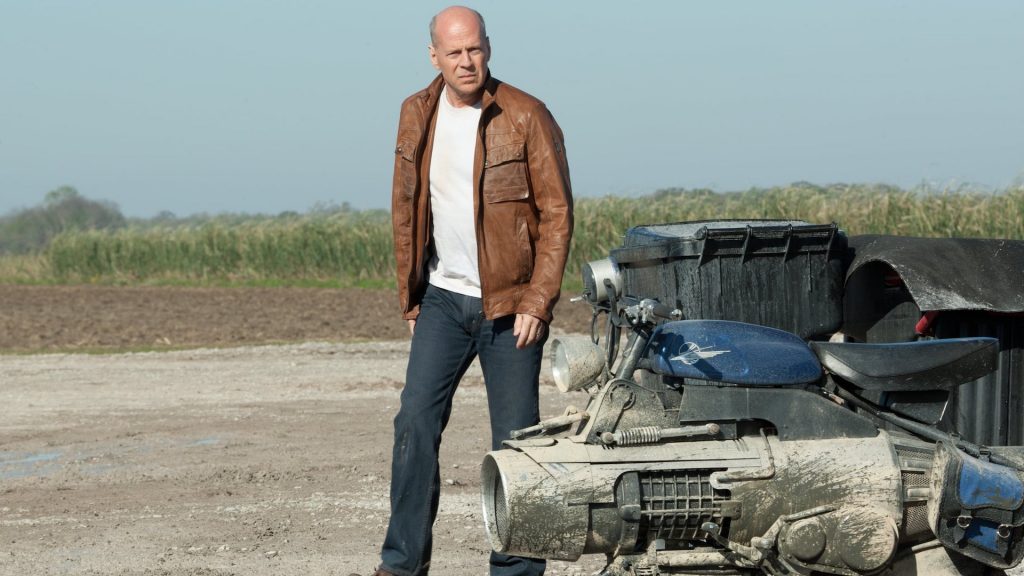 Bruce Willis walks toward a futuristic motorcycle in Looper