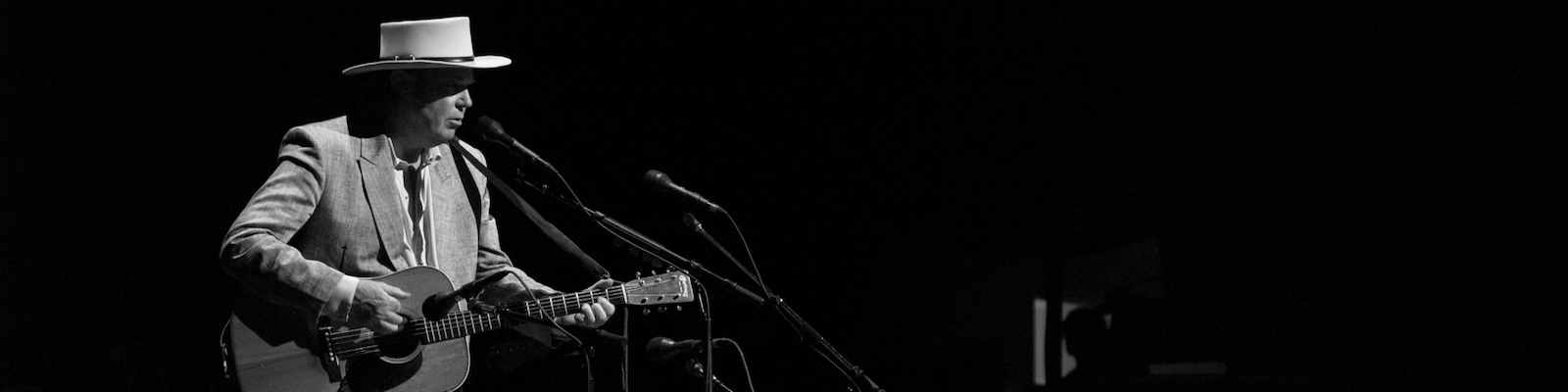 Neil Young sings into a microphone as he plays an acoustic guitar