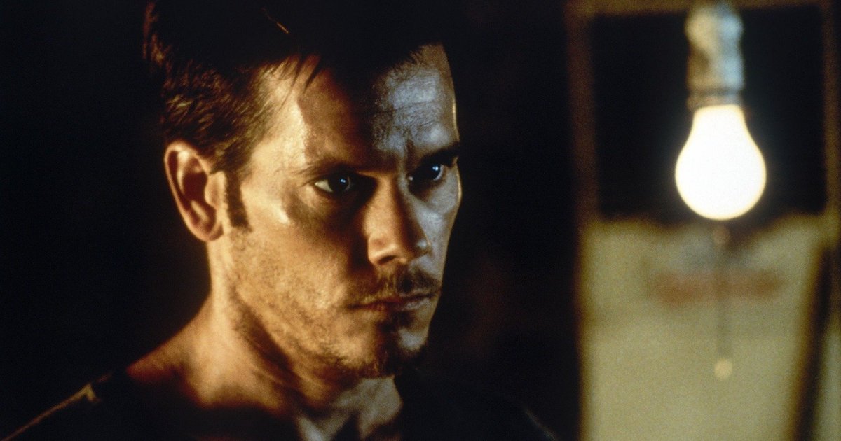 A serioius-looking Kevin Bacon stands near a single hanging, uncovered lightbulb in Stir of Echoes