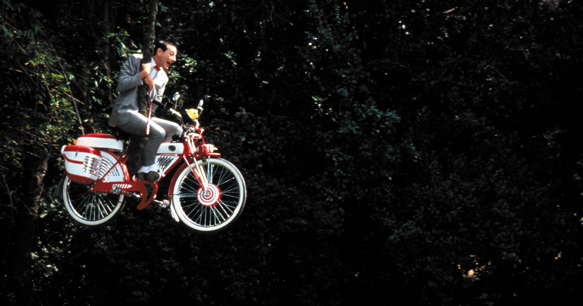 Paul Reubens as Pee-Wee Herman swings across a gorge on his bike while hanging from a vine in Pee-Wee's Big Adventure