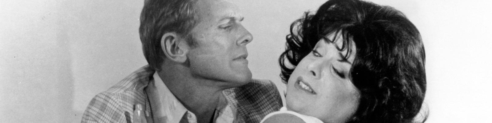 Tab Hunter embraces Divine, who appears to be pulling away from the poster art for Polyester