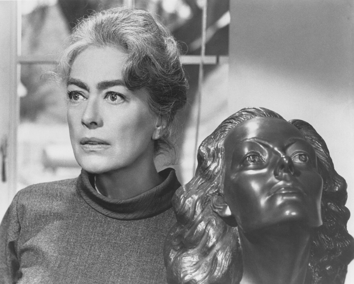 Joan Crawford stands next to a sculpture of a woman's head in Strait Jacket