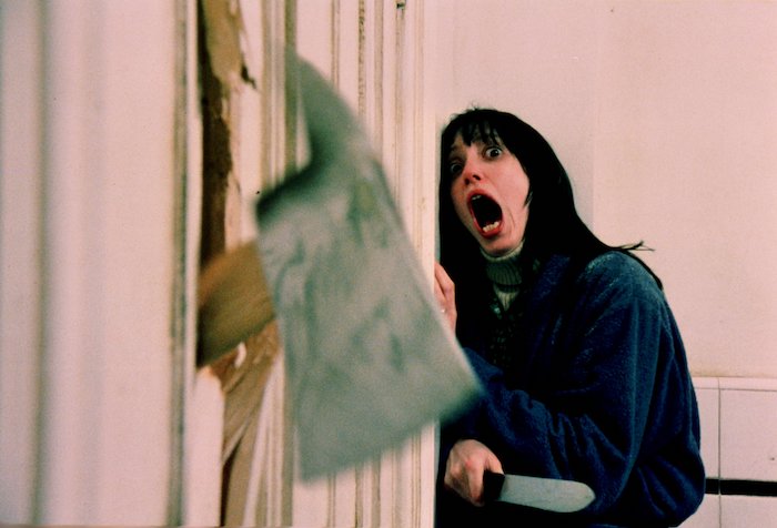 Wendy Torrence (Shelley Duvall) screams in fear as an axe breaks through a door in The Shining