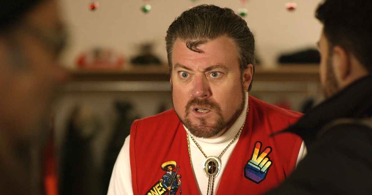 Robb Wells wears a red vest with a pride patch and a bolo tie in Vandits