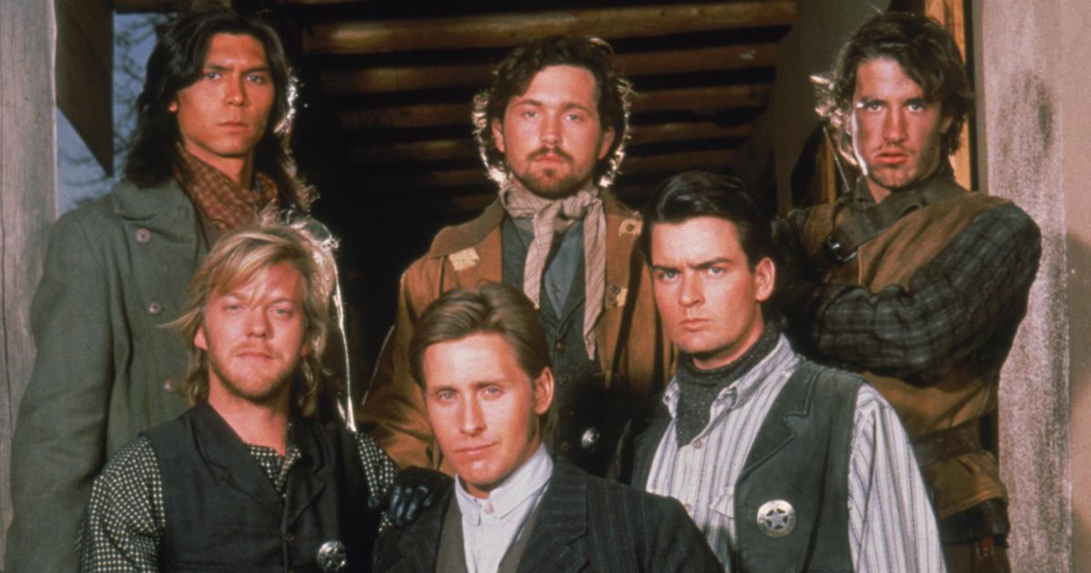 Six twenty-something men pose in two rows for the camera in period "old west" clothing. The men i the front row appear clean and tidy and wear sheriffs stars. The men in the back row wear shabbier clothes and one is noticeably dirty. Promotional image from the film Young Guns